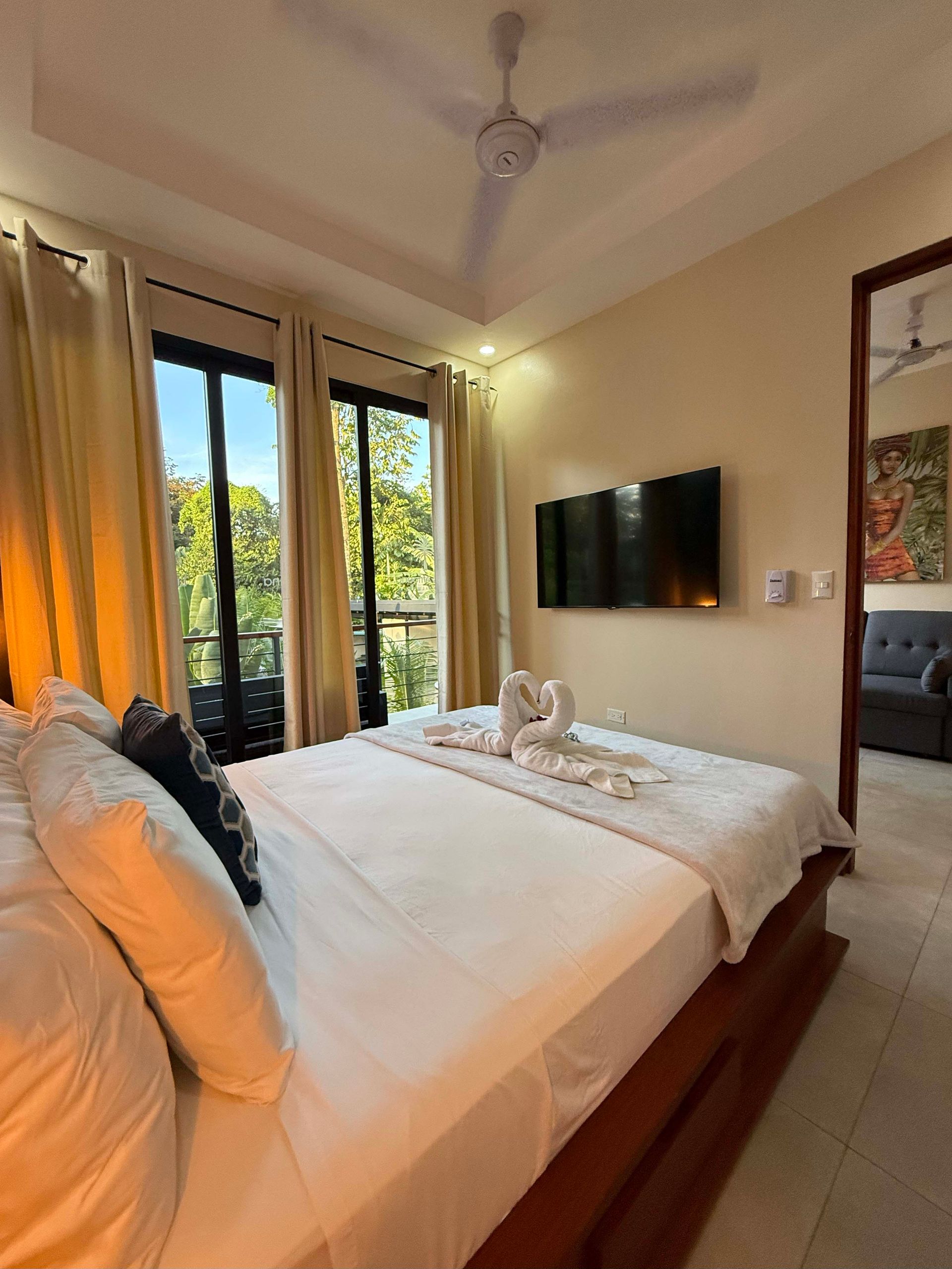 Bedroom with large bed, TV, balcony access, and two towel swans.