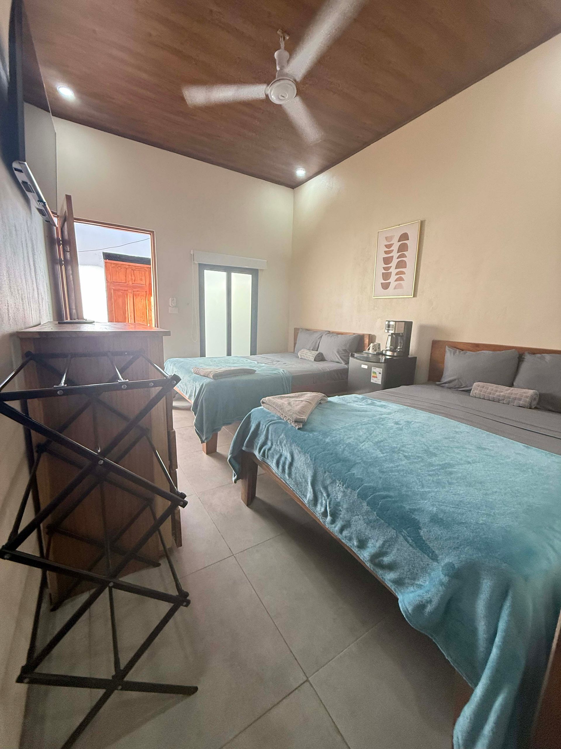 Bedroom with three beds, wooden ceiling and floors, a luggage rack in the foreground.