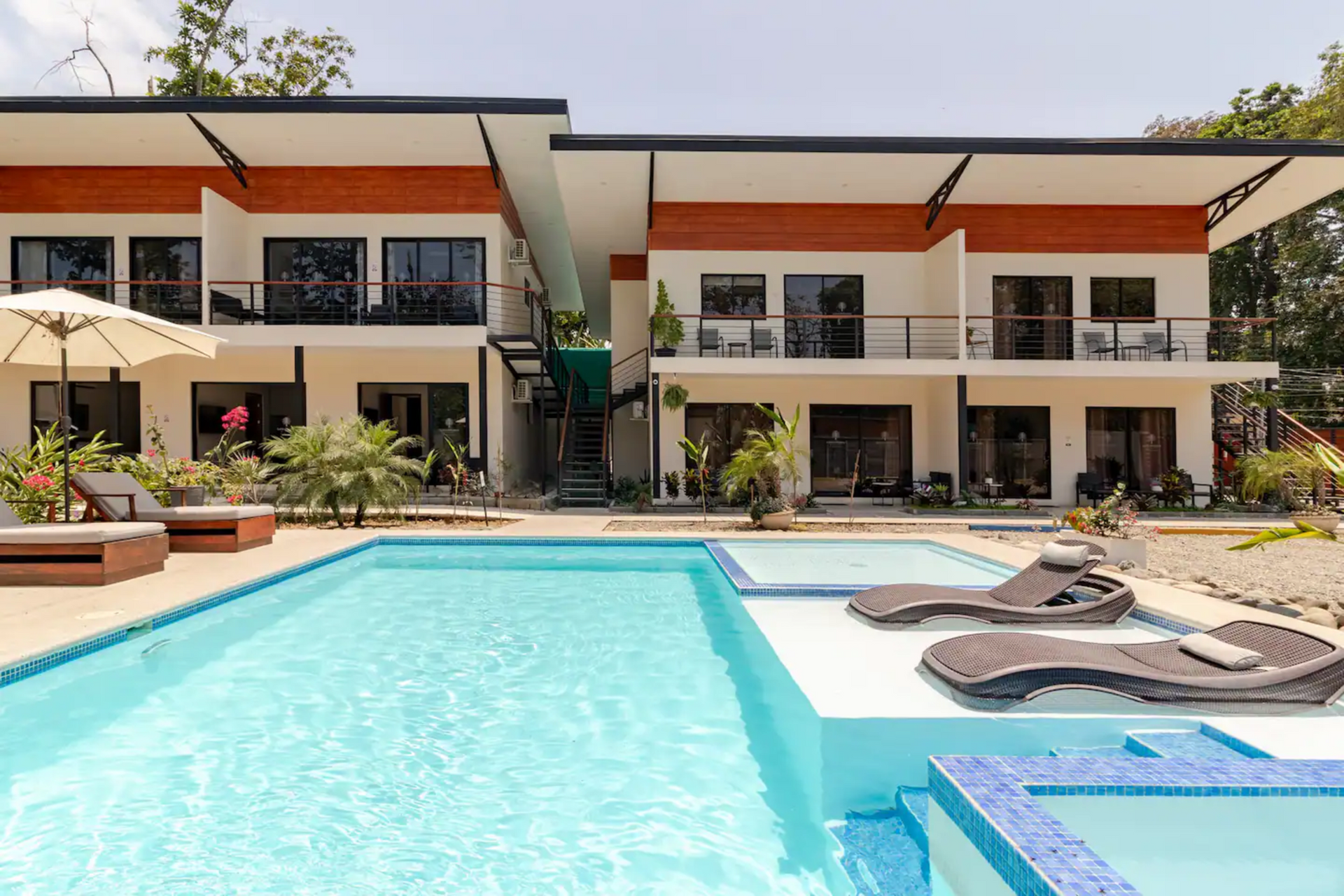 Swimming pool in front of a modern two-story building with lounge chairs.