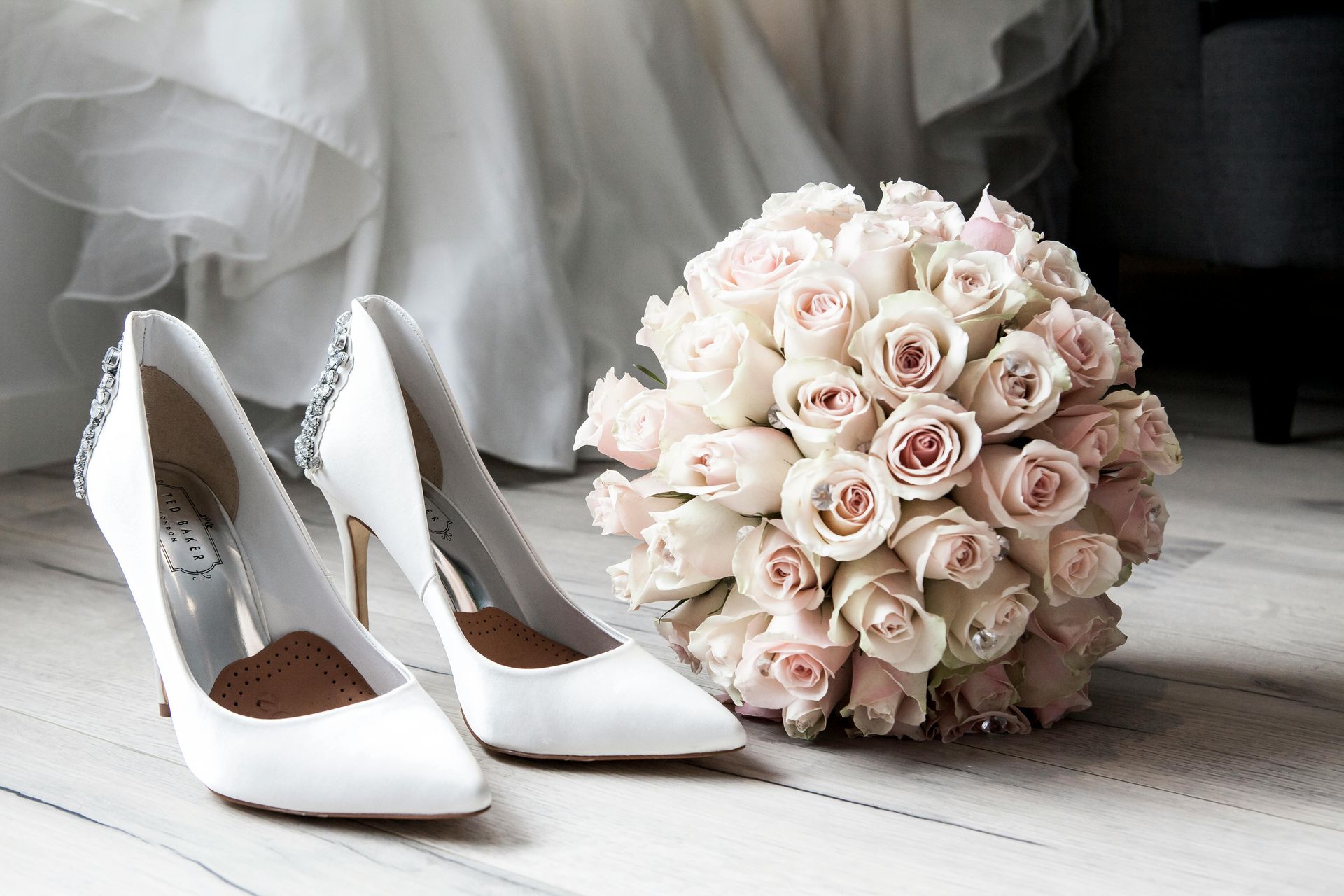 White wedding shoes next to a bouquet of pink and white roses.