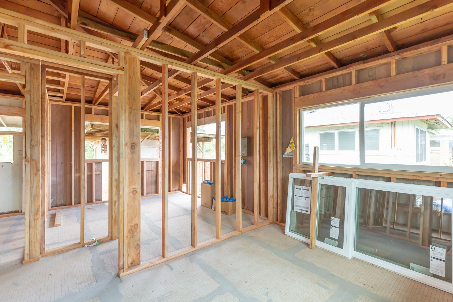 Unfinished room with exposed wooden framing, ceiling beams, and stacked windows in a construction site.