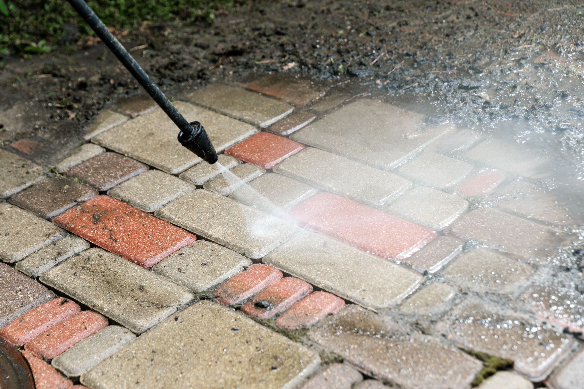 Pressure washing red and tan brick pavers with water spray outdoors