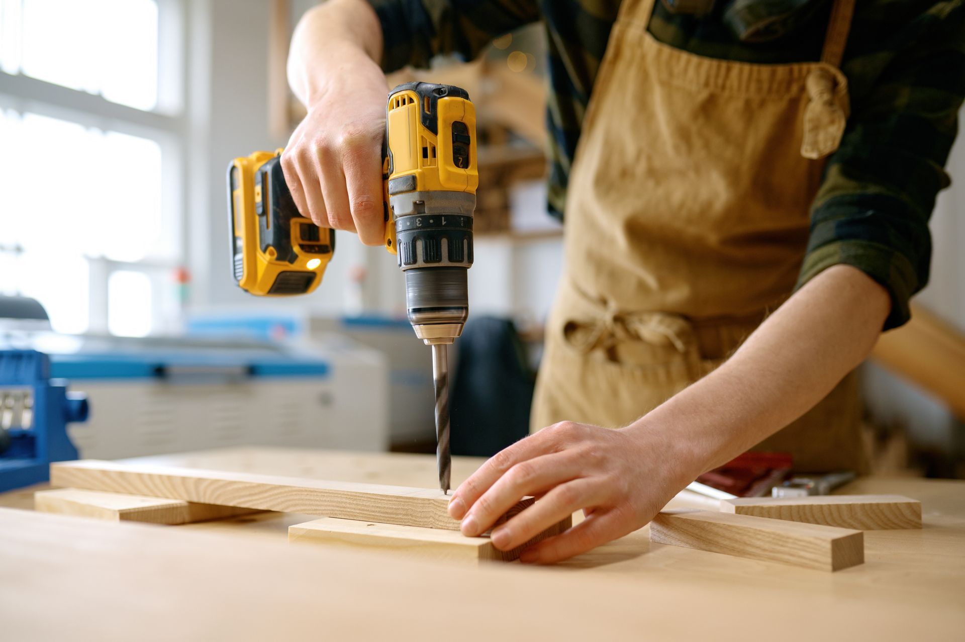 Person drilling a wooden plank on a workbench in a bright workshop