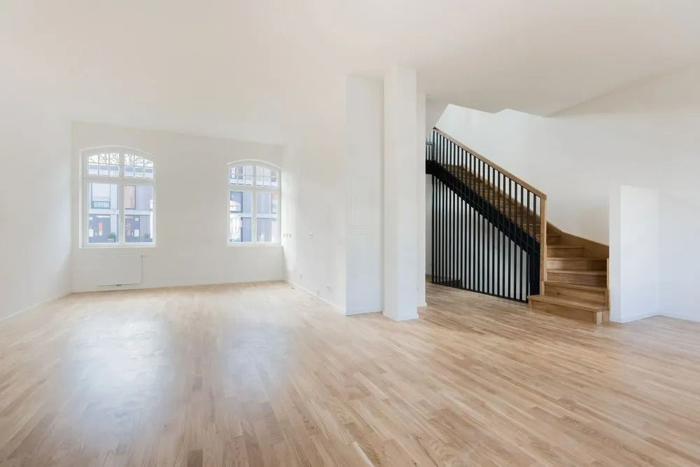 Empty bright living room with light wood floors, white walls, and a staircase on the right