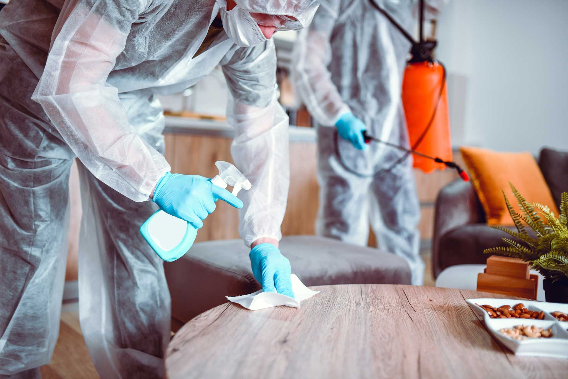Workers in full protective gear performing a biohazard cleanup in a residential living space.