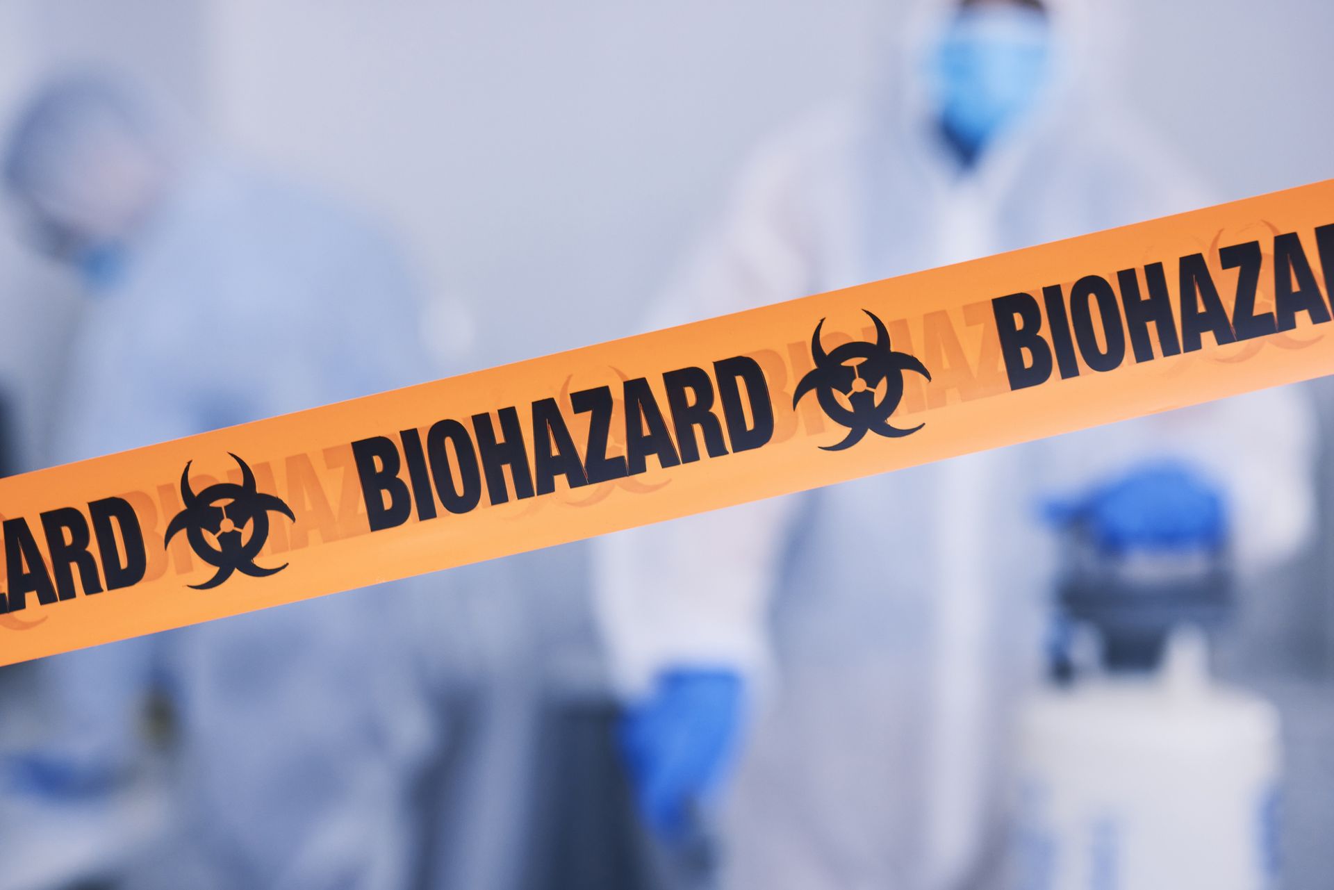 Close view of a yellow biohazard tape with uniformed people in the background.