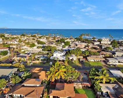 Aerial view of a coastal town with houses and palm trees, the ocean in the background under a blue sky.