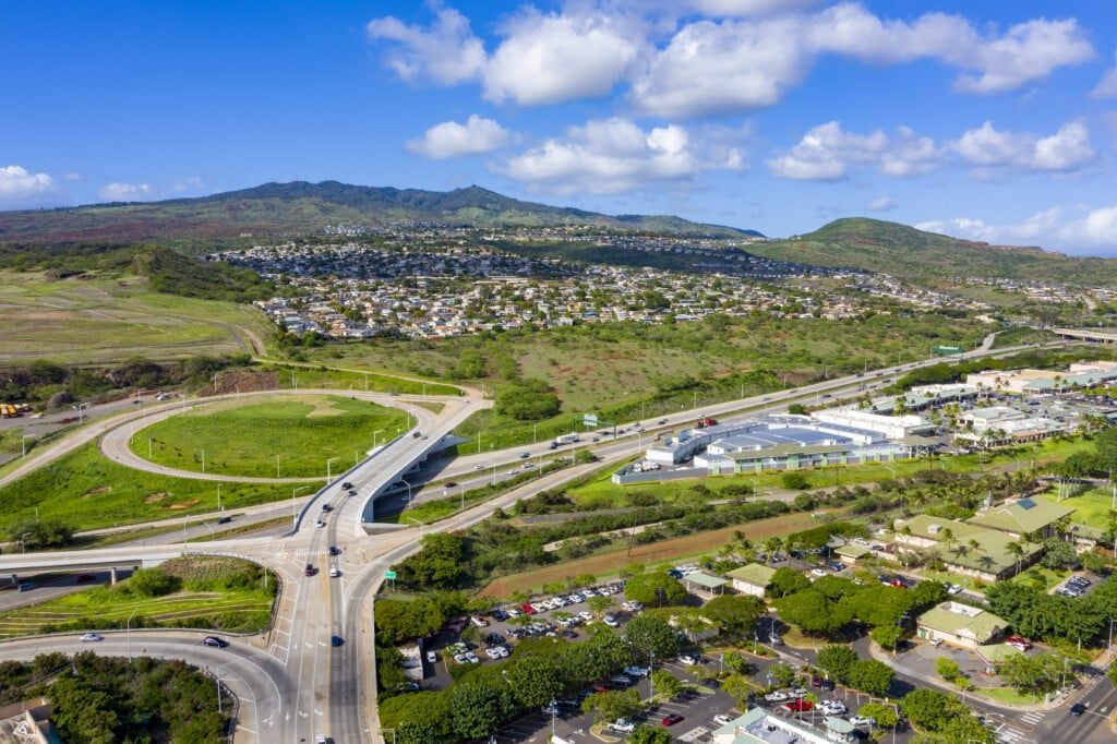 Aerial view of a highway overpass, suburban homes, and a mountain under a partly cloudy sky.