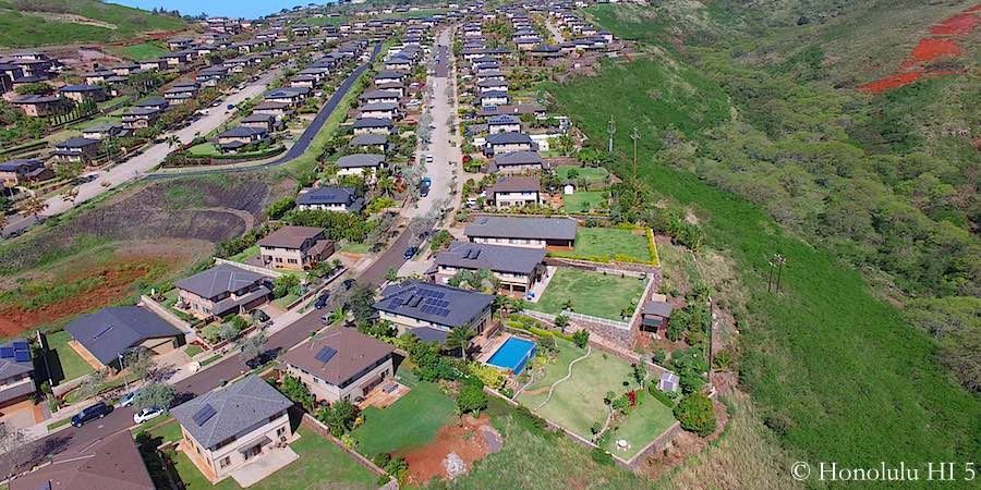 Aerial view of houses nestled on a hillside with lush green vegetation and a road running through the neighborhood.