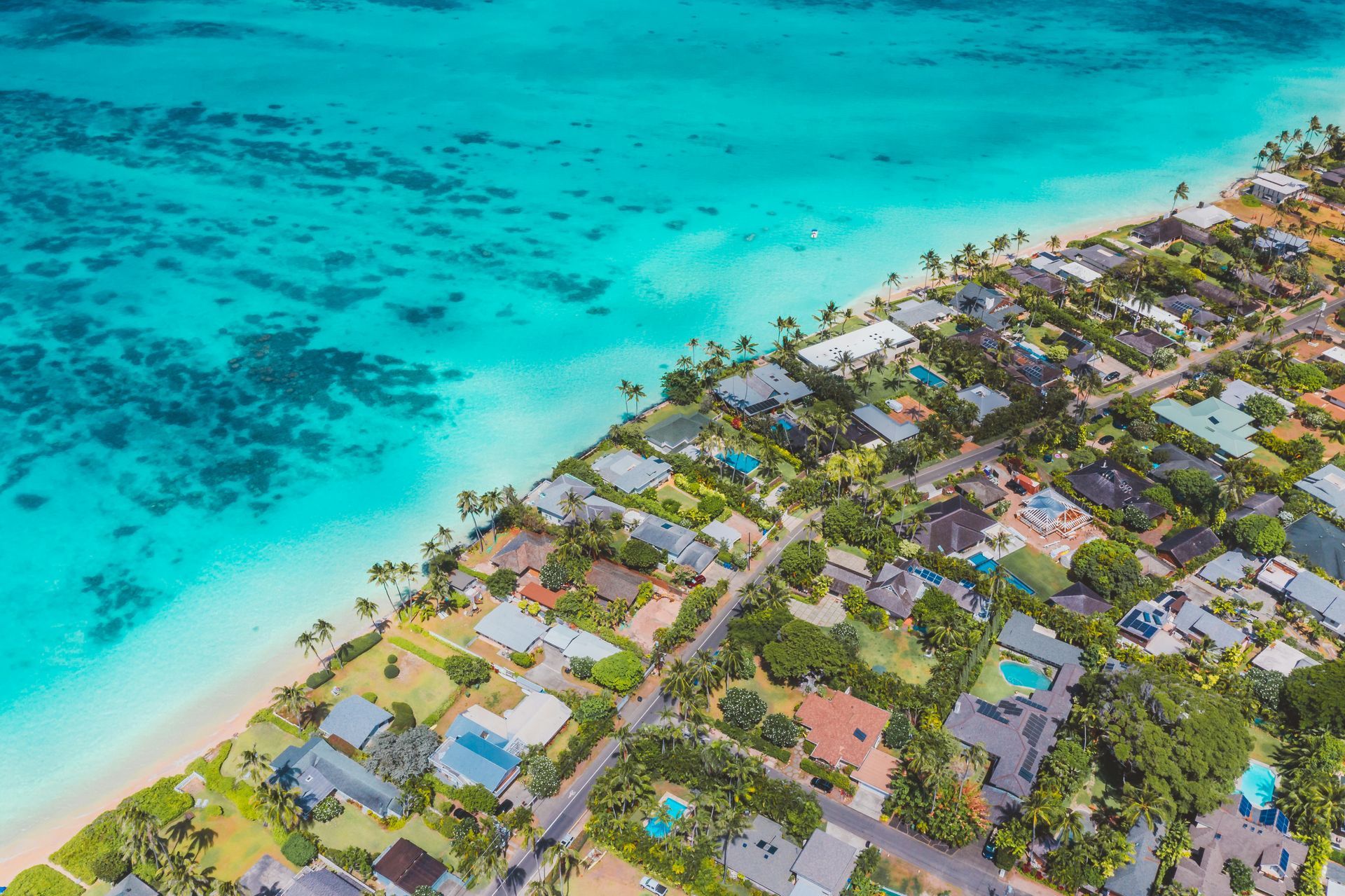 Aerial view of a coastal community with turquoise water, sandy beach, and houses with green yards.
