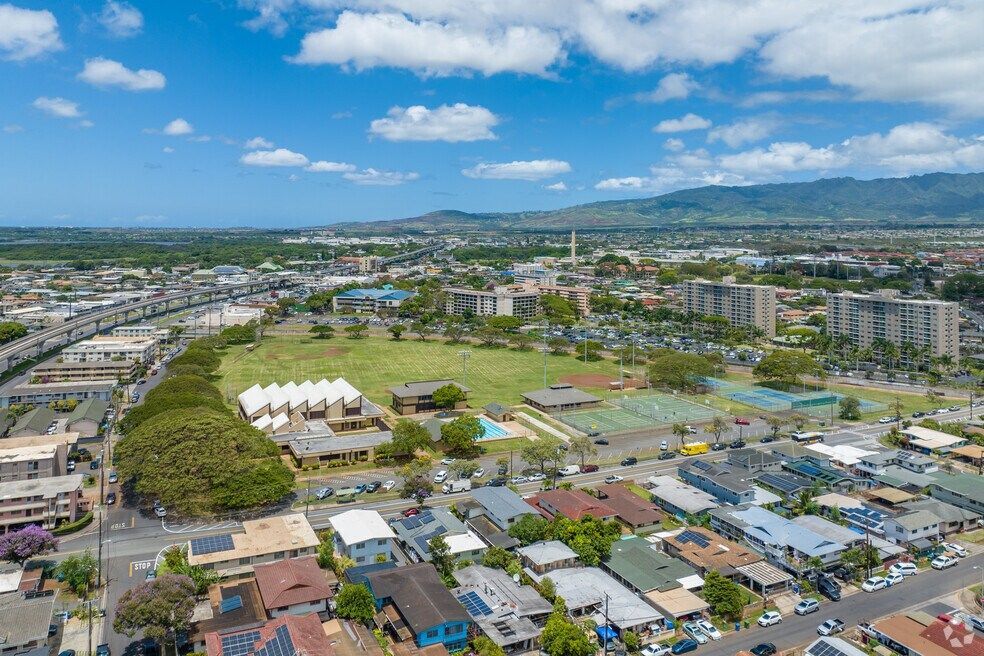 Aerial view of a city with residential buildings, a park, and mountains under a blue sky.