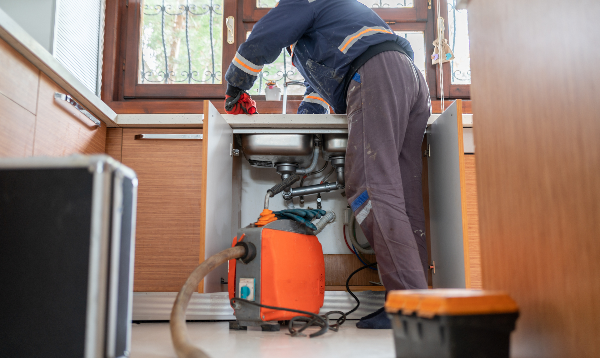 A plumber is using a vacuum cleaner to clean a sink in a kitchen.