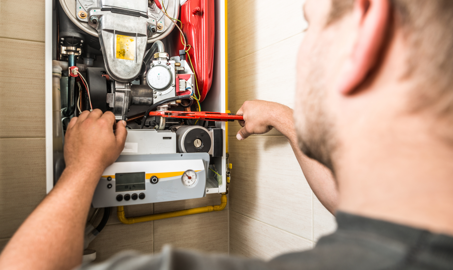A man is fixing a boiler with a wrench.