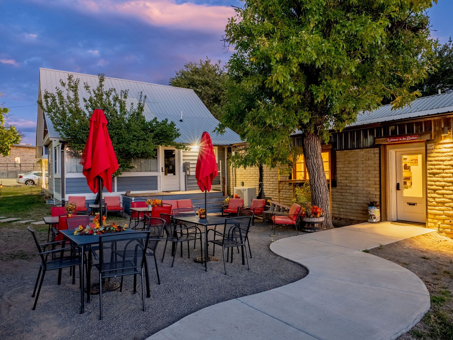 A patio with tables and chairs and red umbrellas in front of a house.
