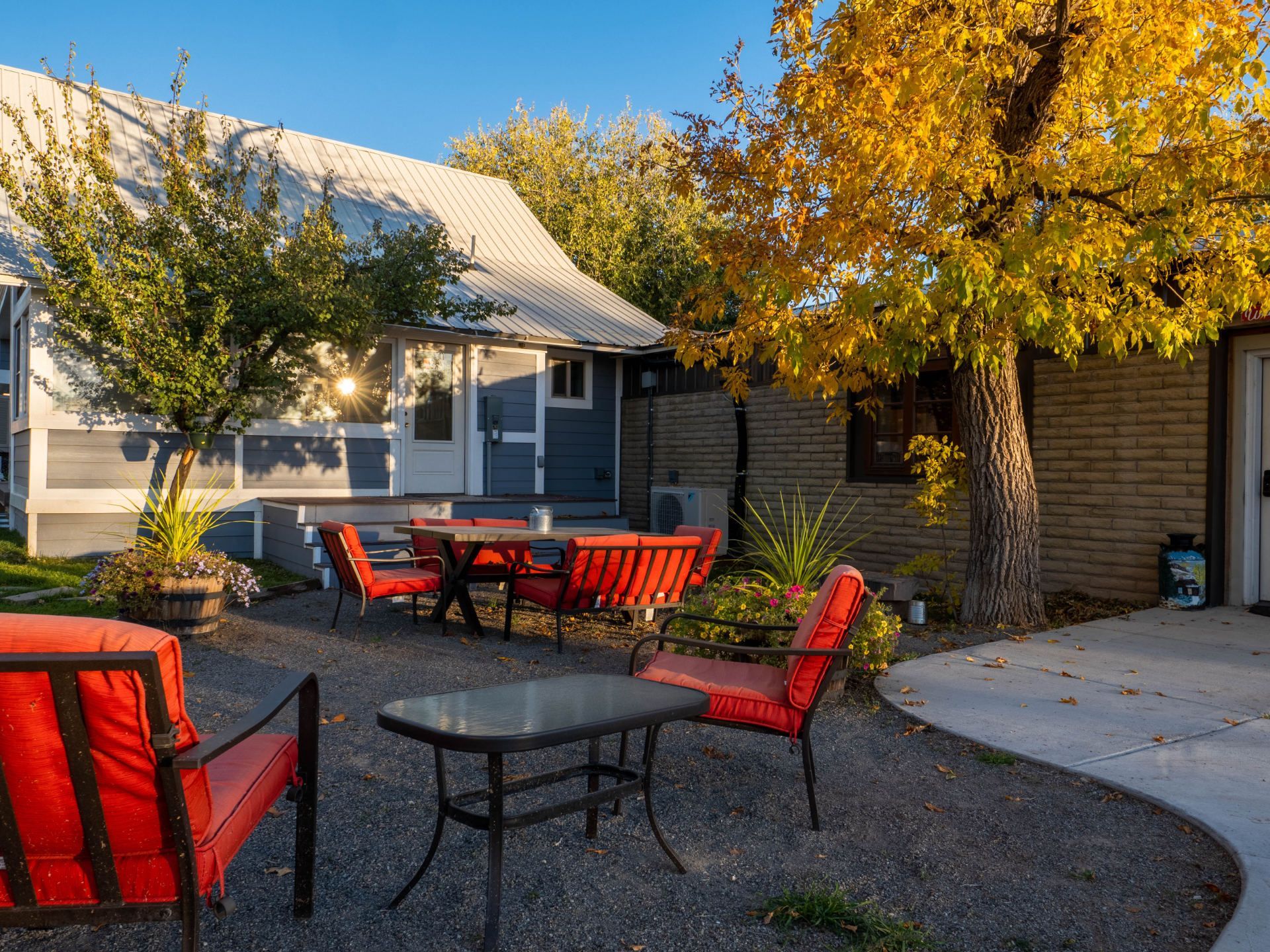 A patio with tables and chairs and red umbrellas in front of a house.