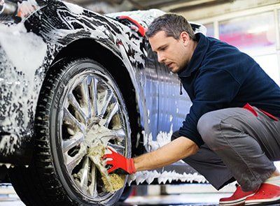 Man crouched down sponge washing alloy wheels car covered in suds