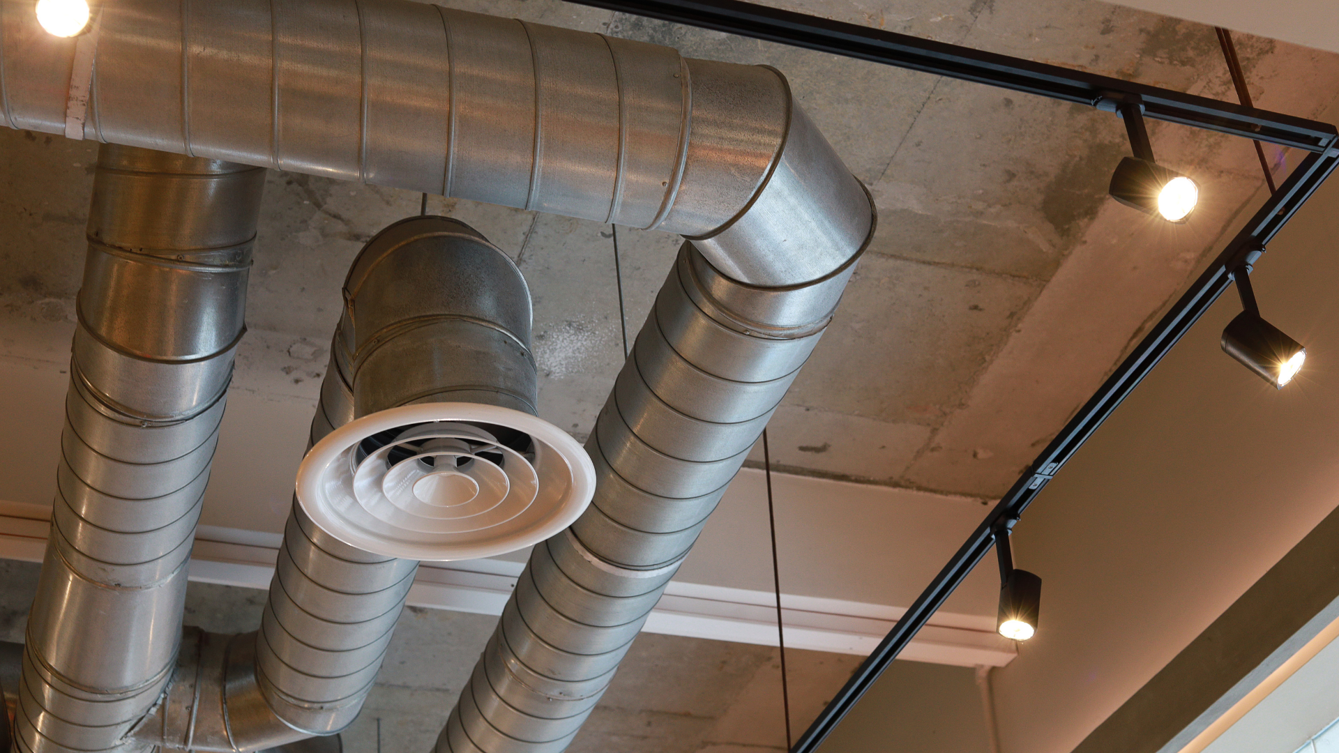 Metal air ducts and track lighting on a concrete ceiling.