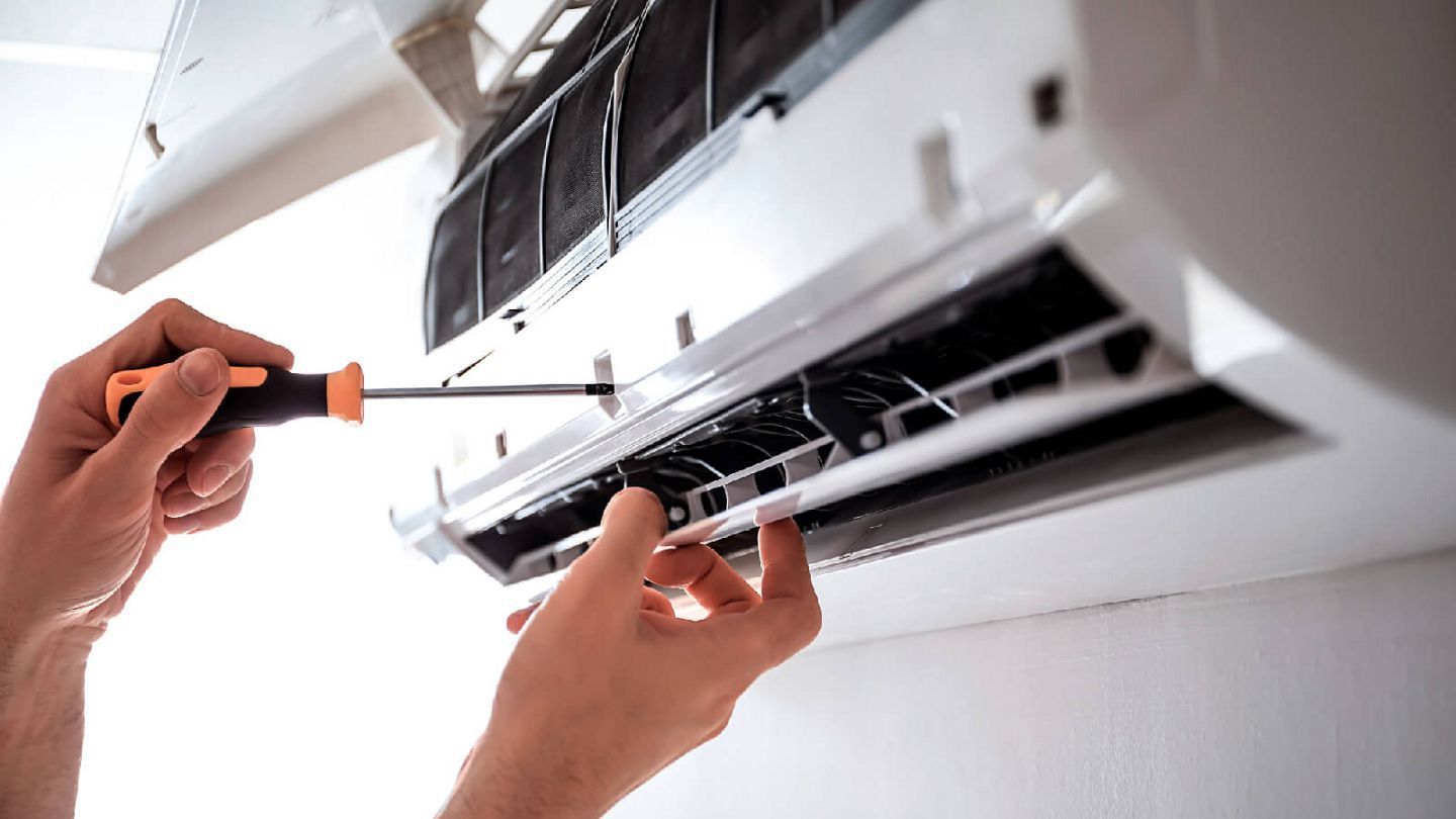 Person using a screwdriver to repair a white air conditioning unit.
