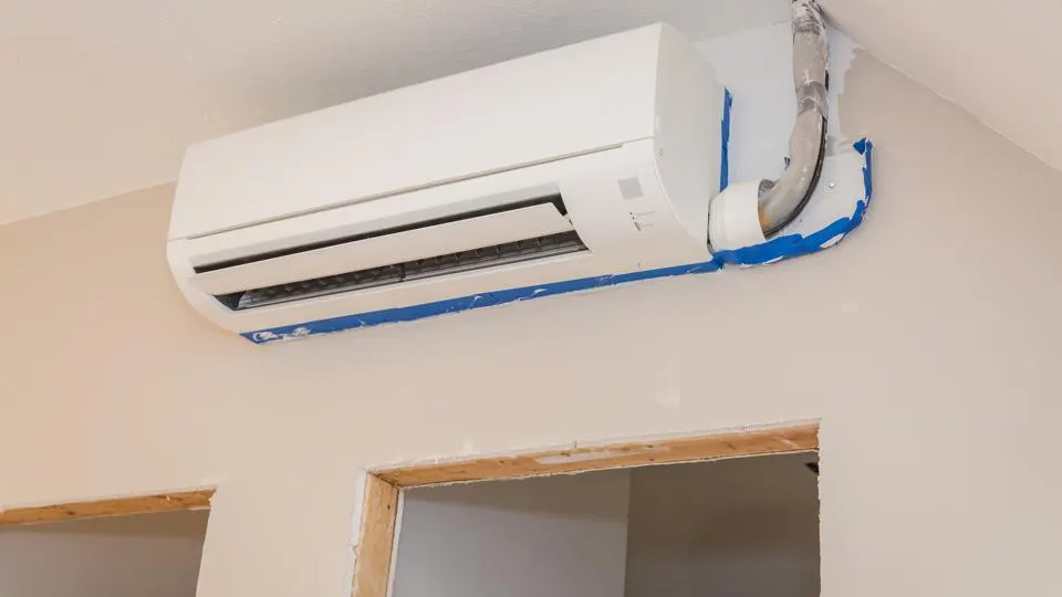 White wall-mounted air conditioner unit installed on a beige wall, next to a doorway.