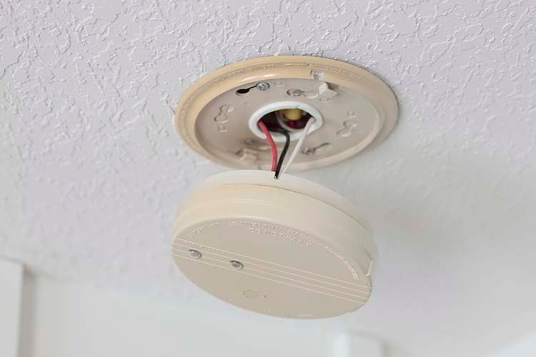 Smoke detector detached from ceiling, exposing wires.