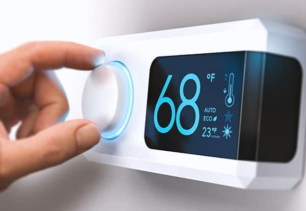 Hand turning dial on a digital thermostat, setting it to 68 degrees Fahrenheit.