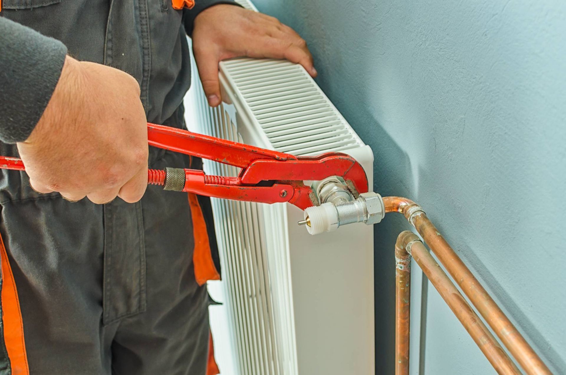 Plumber using pliers to work on a copper pipe connected to a radiator in a room.