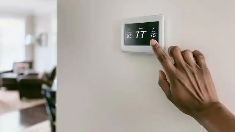 Hand adjusting a smart thermostat; setting is 75 degrees Fahrenheit.
