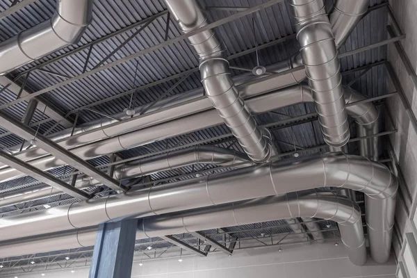 Silver HVAC ductwork installed on a gray ceiling, angled and curved, in a commercial building.