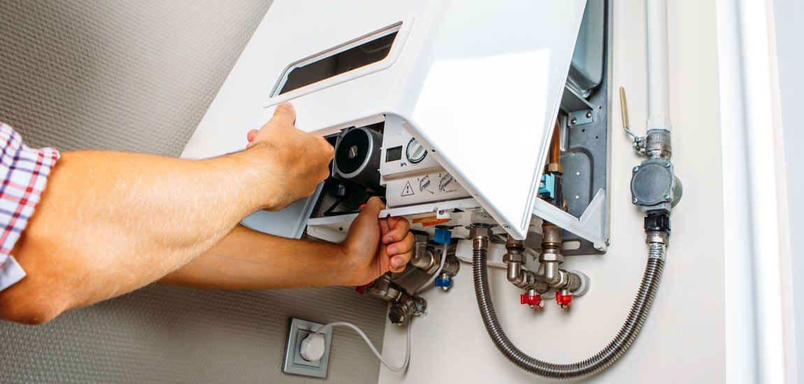 A person is working on a white heating unit installed on a wall.