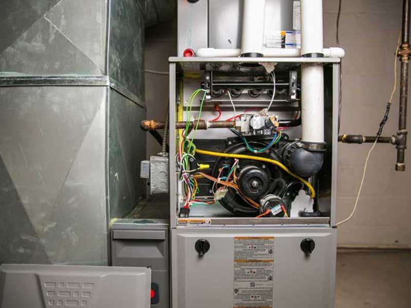 Furnace with open panels showing internal components, including wires, blower, and pipes.