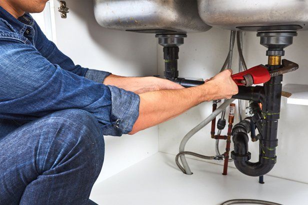 Plumber with wrench working under kitchen sink.
