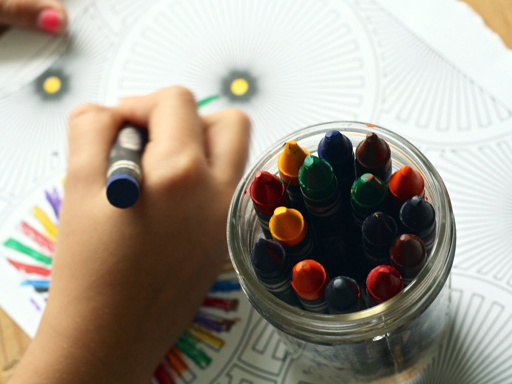 A child drawing with a crayon next to a jar of crayons