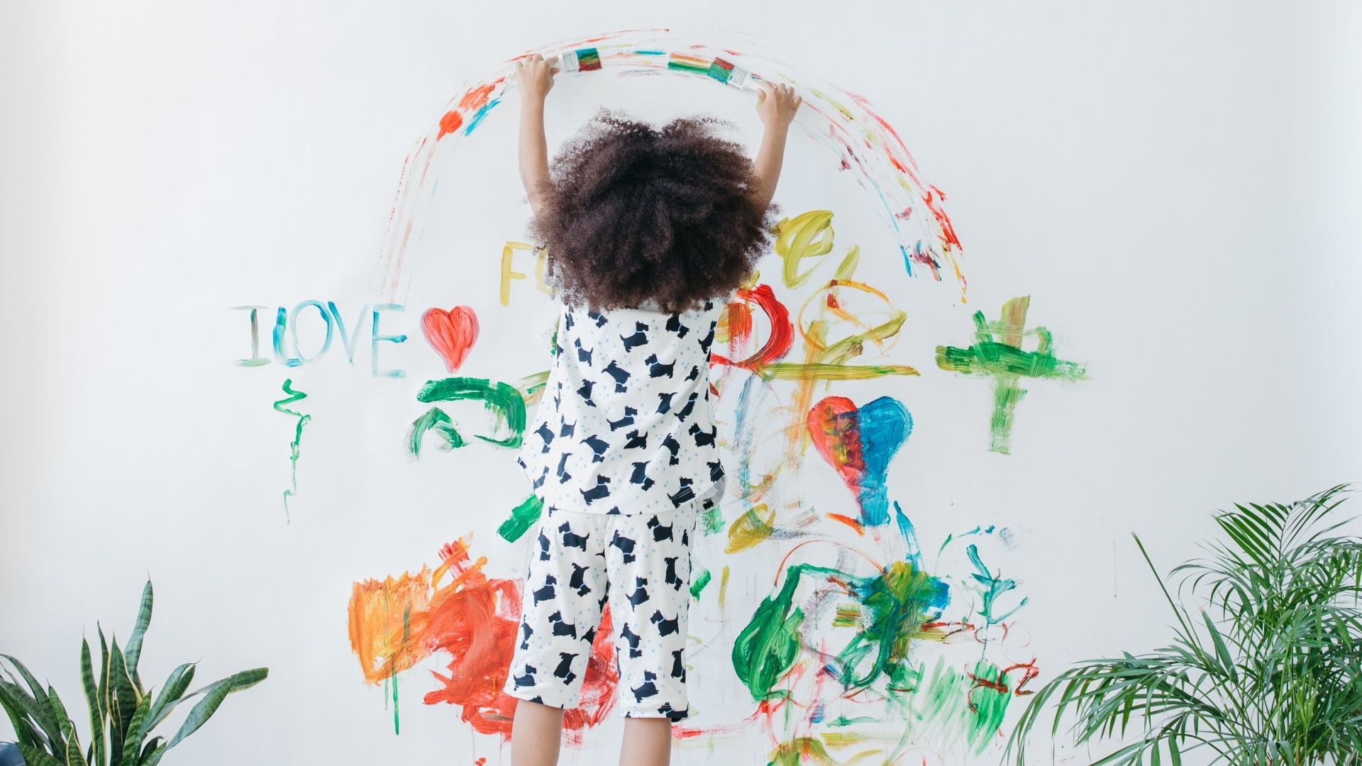 A little girl is standing in front of a wall covered in paint.