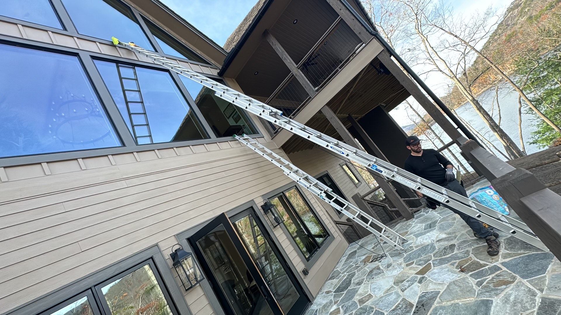 A man is standing in front of a large house with a ladder attached to it.