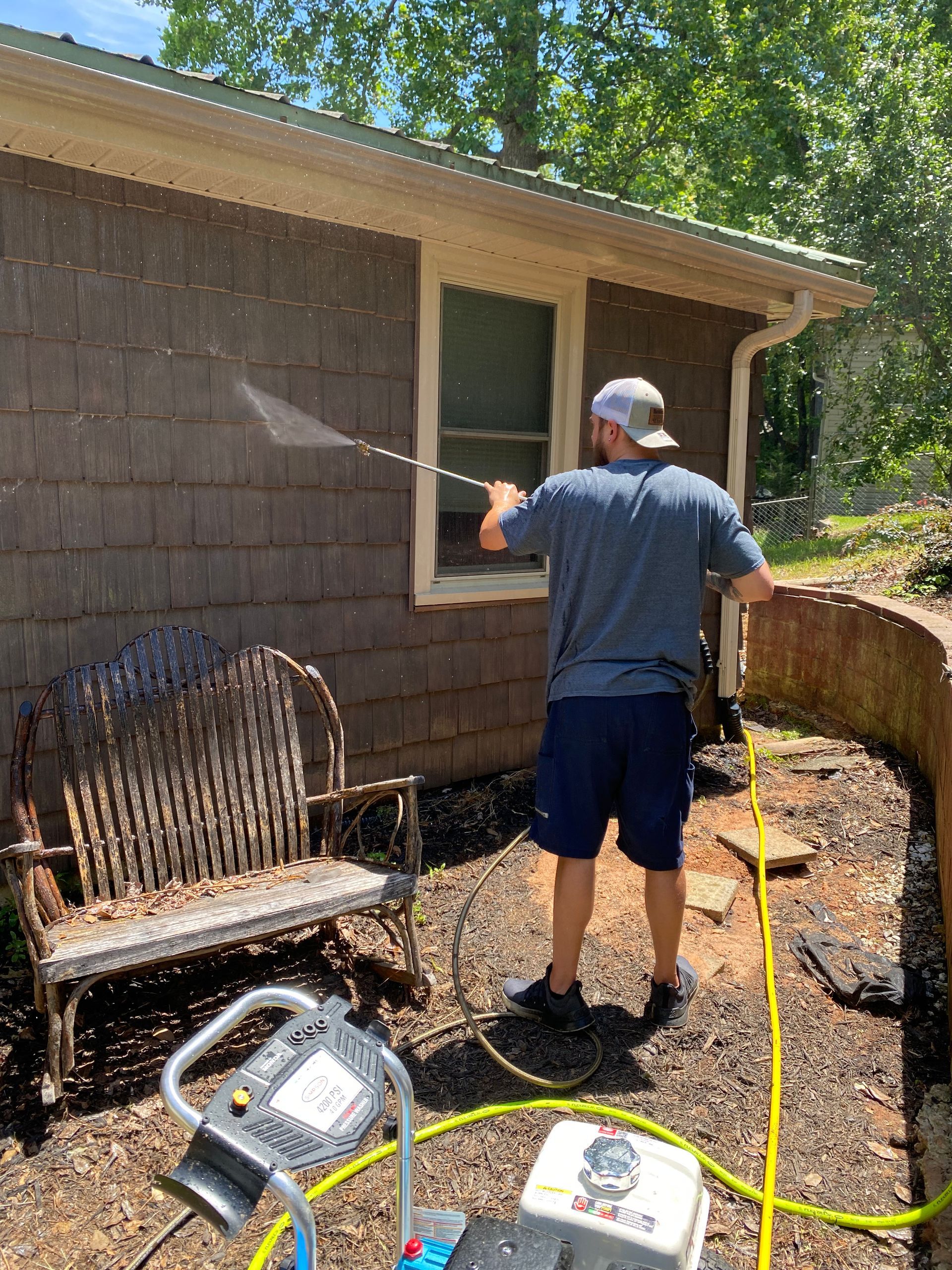 A man is cleaning the side of a house with a high pressure washer.