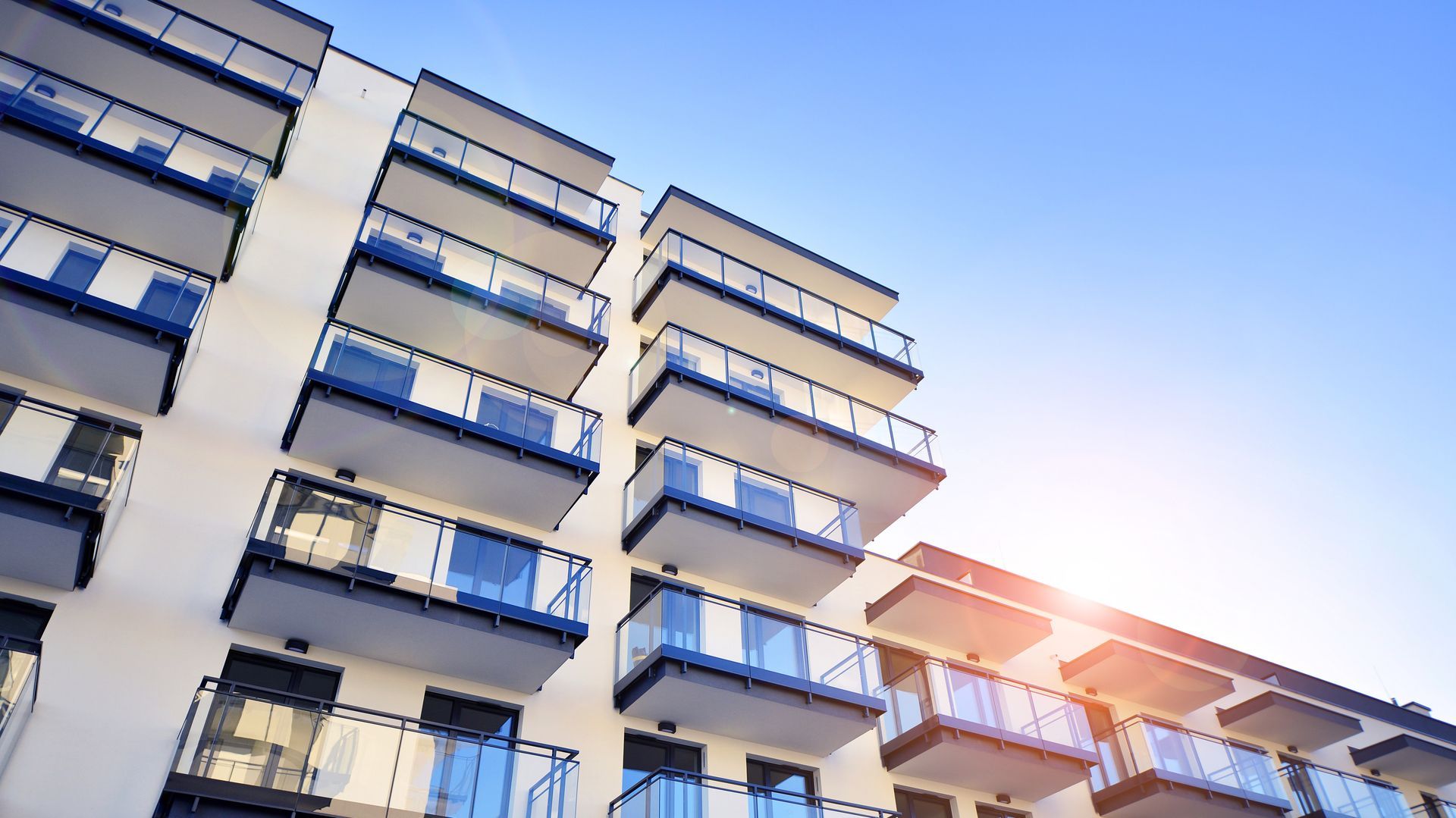 A large apartment building with lots of balconies against a blue sky.
