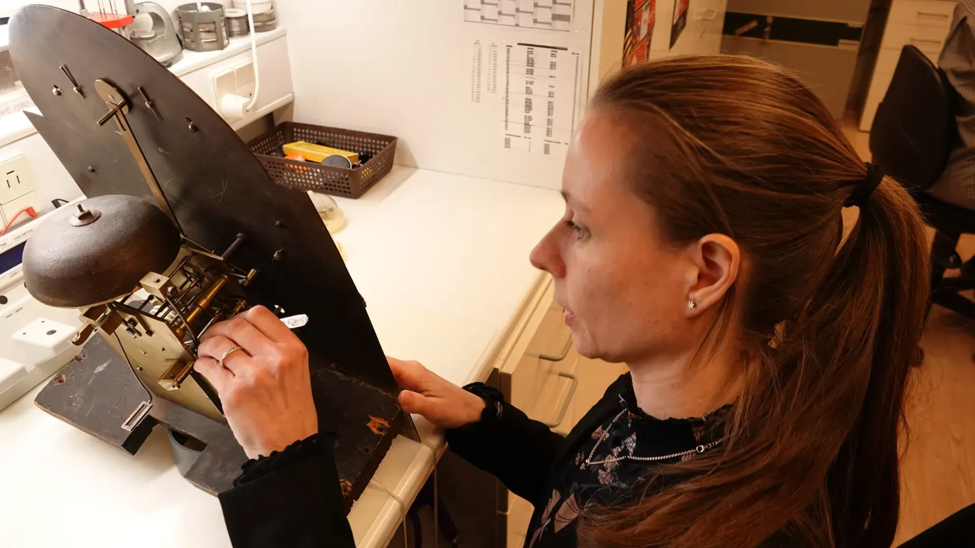 Kvinde i laboratoriekittel justerer et mikroskop i et lyst laboratorium.