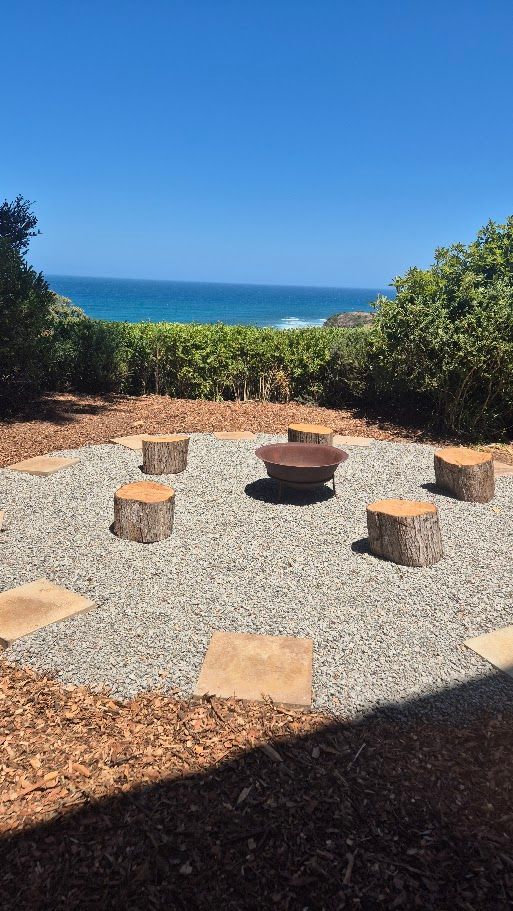 There is a fire pit in the middle of the yard with a view of the ocean.