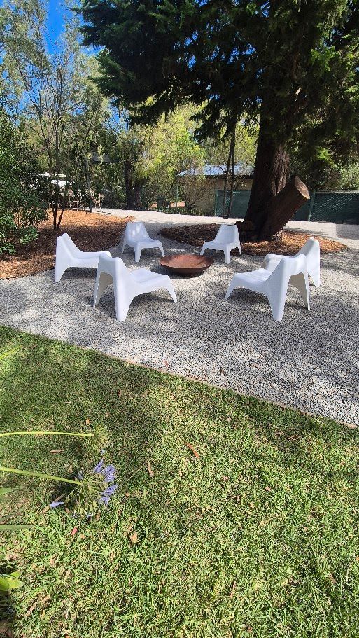 A group of white chairs are sitting around a fire pit in a yard.