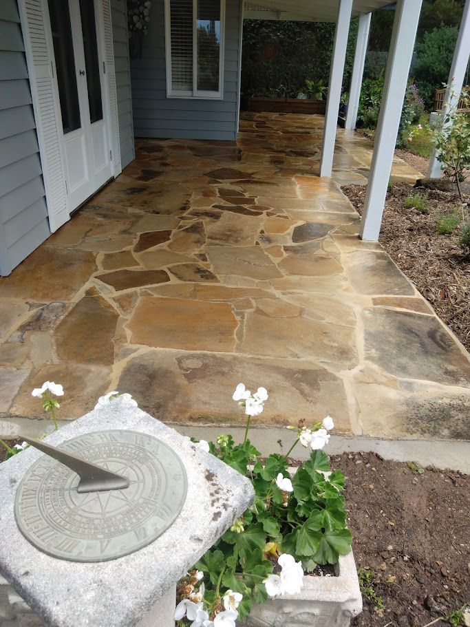 A stone patio with flowers and a sundial in front of a house.