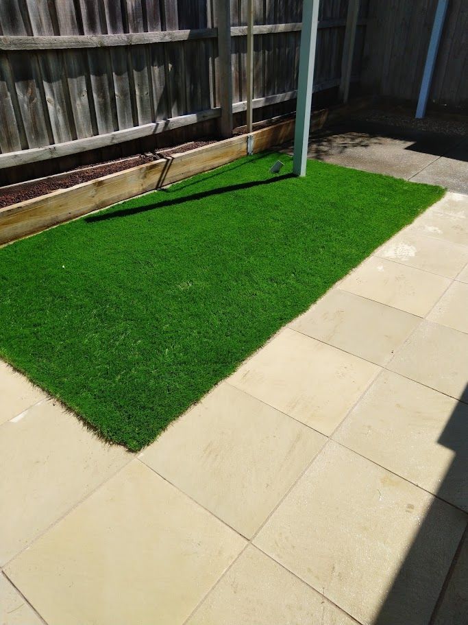 A patch of green grass on a patio next to a fence.