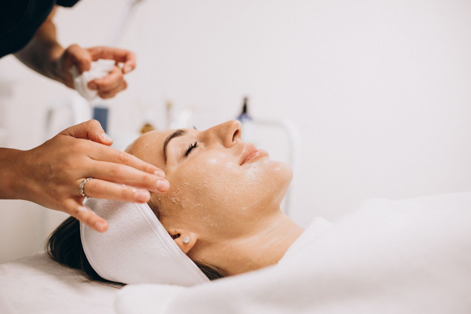 Woman receiving a facial treatment at a spa, lying down with eyes closed, in a white room.