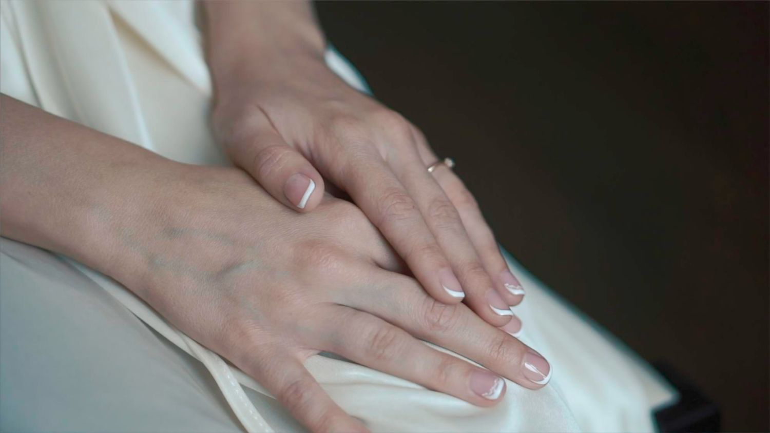 Hands resting gently on a white fabric lap.