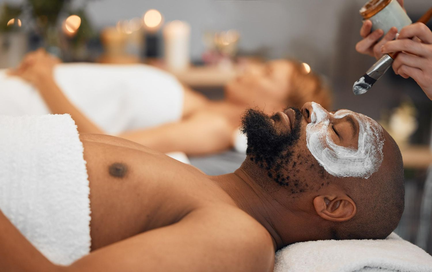 Man receiving a facial treatment with cream applied, lying on a spa bed in a relaxing setting