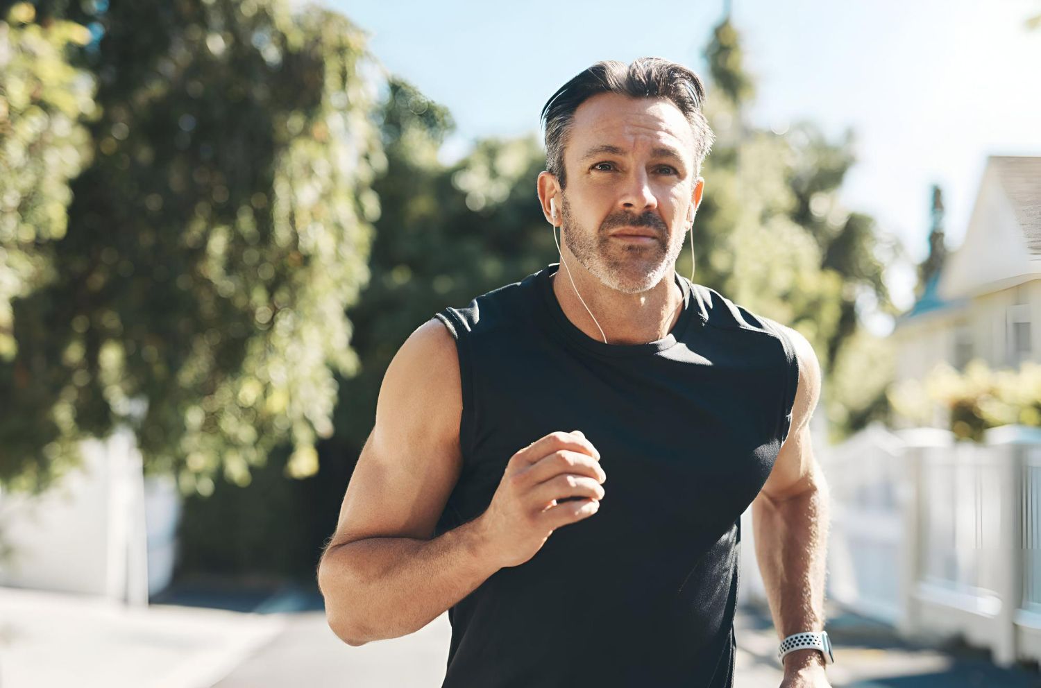 Man jogging outdoors in a black sleeveless shirt on a sunny residential street