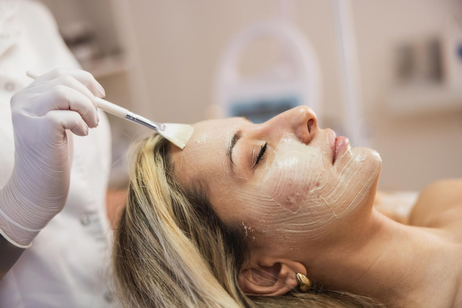 Facial treatment being applied with a brush to a woman lying on a spa bed
