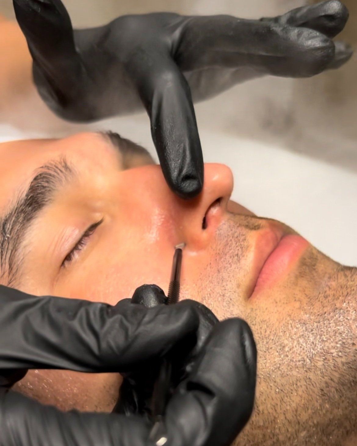 A man is getting a facial treatment with black gloves