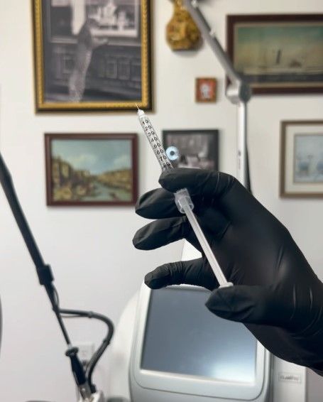 A person wearing black gloves is holding a syringe in their hand