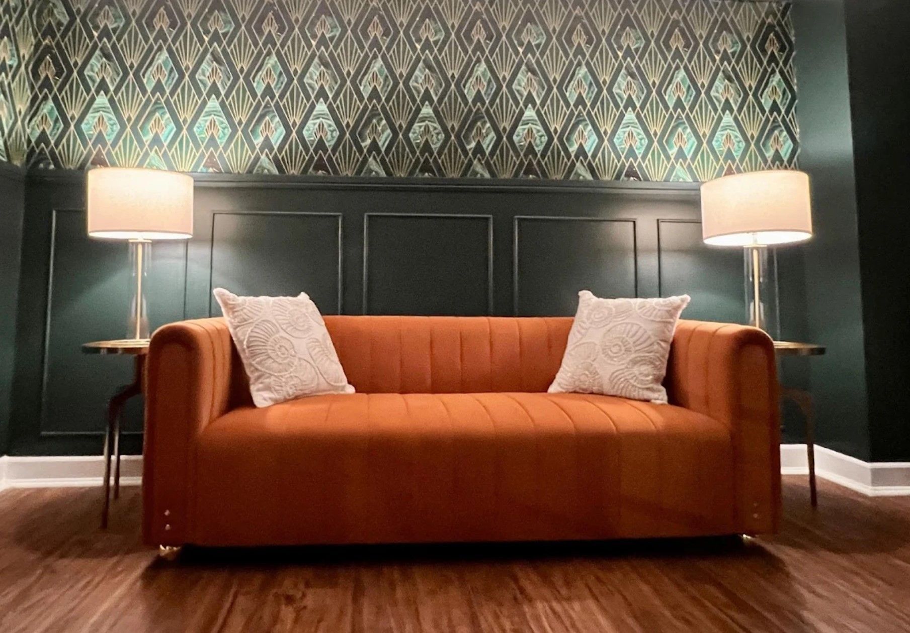 An orange couch is sitting in a living room next to two lamps.