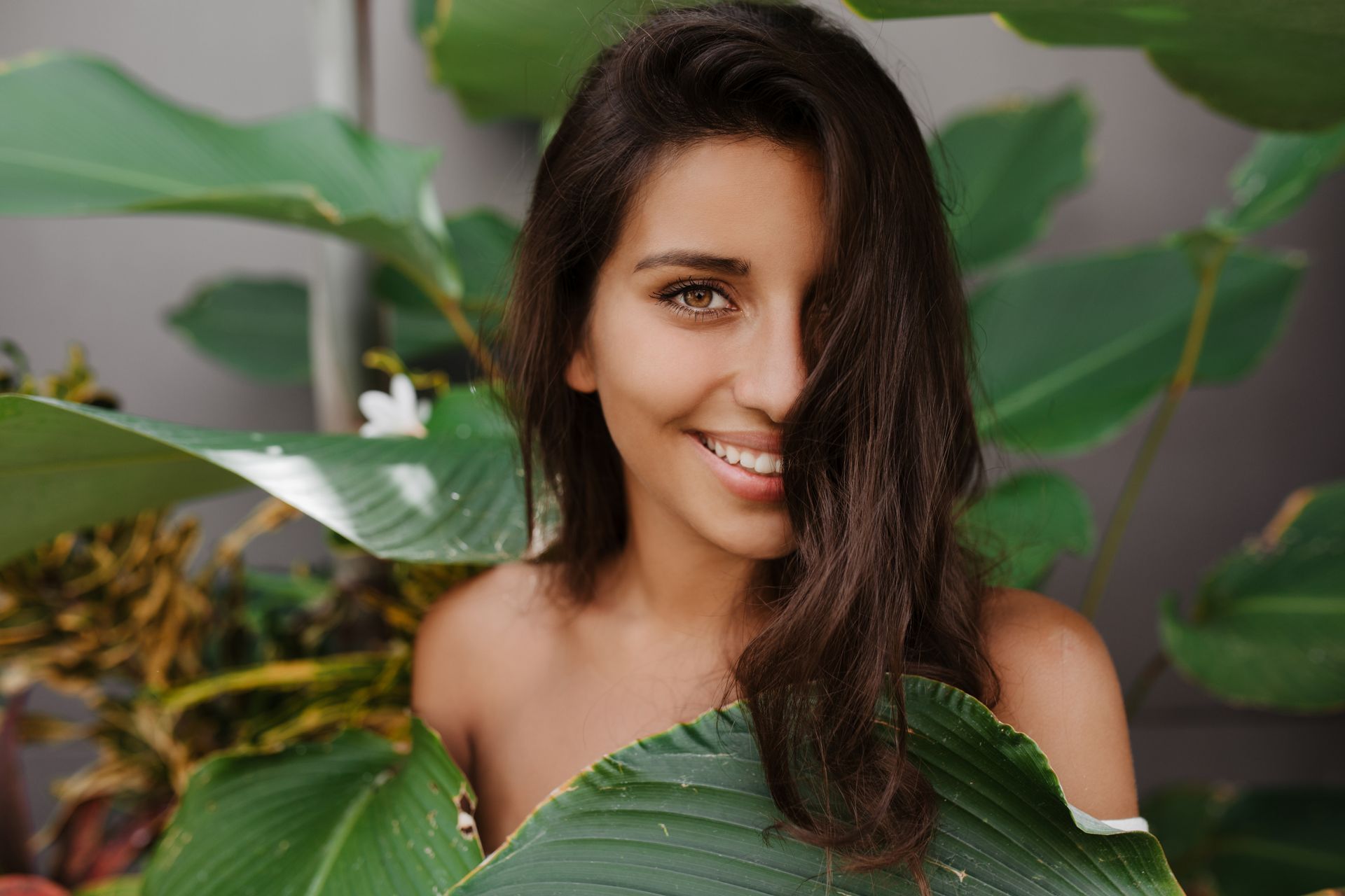 A woman is smiling while holding a leaf in front of her face.